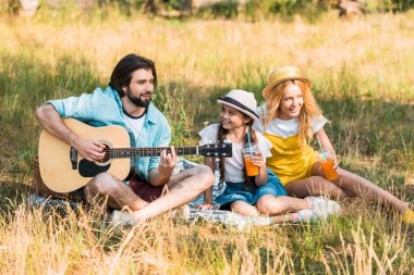yakışıklı baba piknikte kızı ve karısı için akustik gitar çalmak
