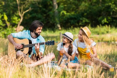 mutlu baba piknikte kızı ve karısı için akustik gitar çalmak