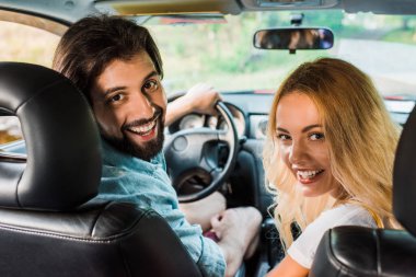 arabada oturan ve kameraya bakarak gülümseyen çift