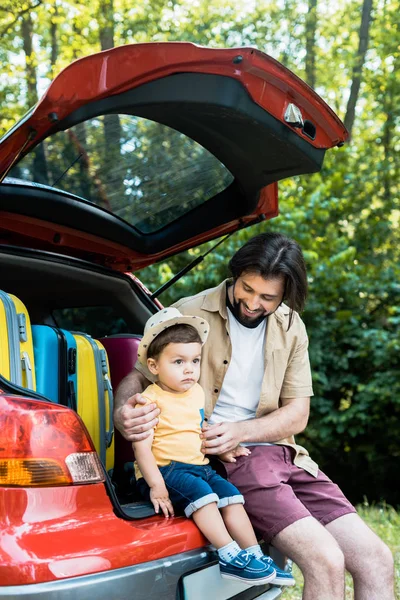 father and son sitting on car trunk in forest