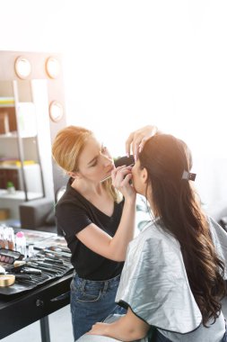 side view of focused makeup artist applying eye shadows on womans eyelid clipart