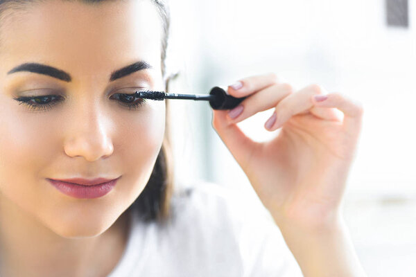 portrait of attractive young woman applying black mascara on eyelashes