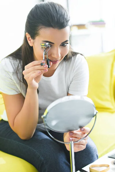 自宅アイラッシュカーラーでまつげをカールしながら鏡を見て若い女性  — 無料ストックフォト