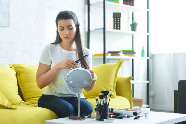 привлекательная женщина расчесывает волосы расческой, сидя дома на диване
