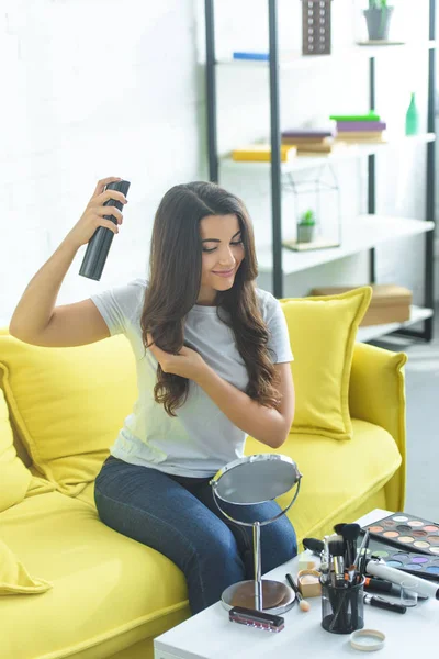 Lachende Vrouw Haarspray Toepassen Voor Positiebepaling Kapsel Zittend Bank Thuis — Stockfoto