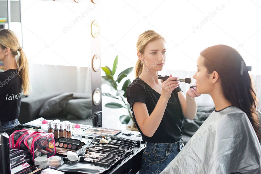 side view of focused makeup artist applying powder on womans face with brush
