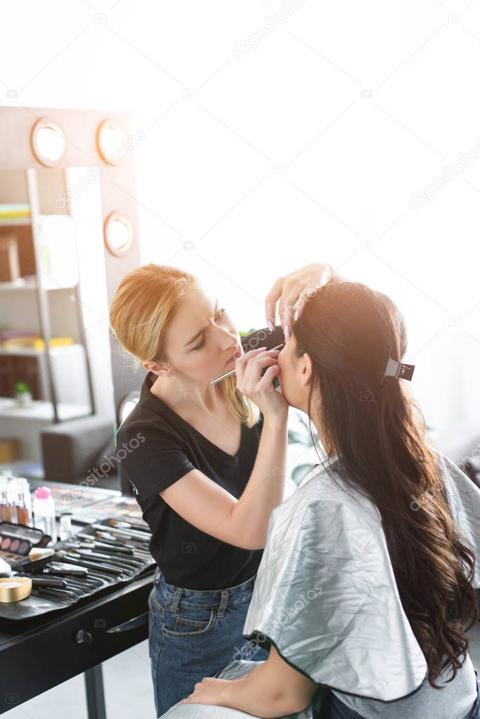 side view of focused makeup artist applying eye shadows on womans eyelid