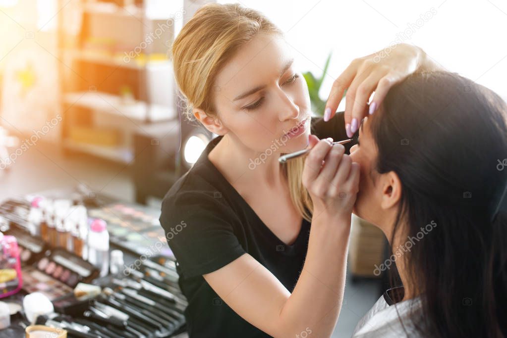 side view of focused makeup artist applying eye shadows on womans eyelid