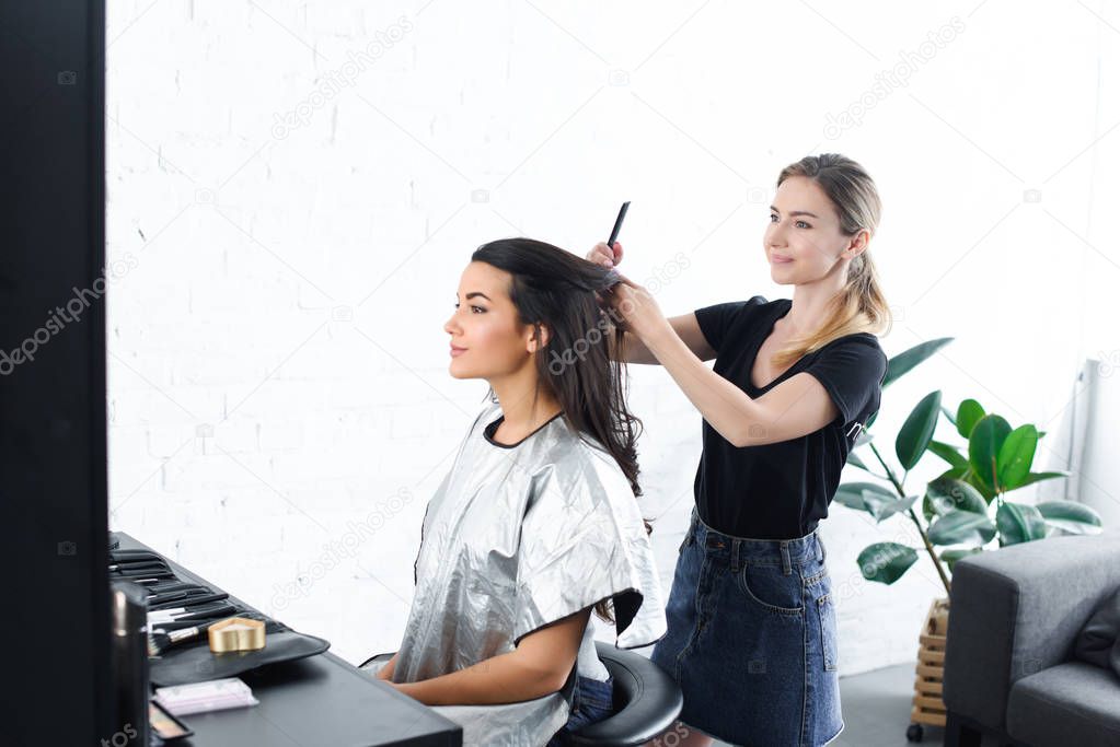 side view of hairstylist with comb doing hairstyle for young woman 