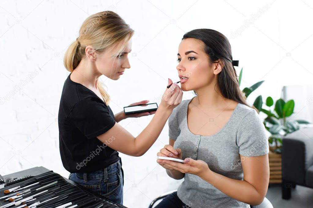 attractive woman with smartphone getting makeup done by makeup artist