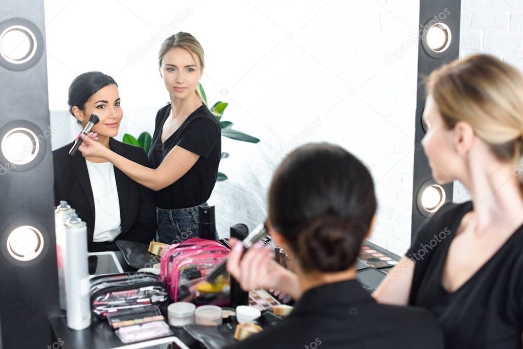 young smiling businesswoman getting makeup done by makeup artist