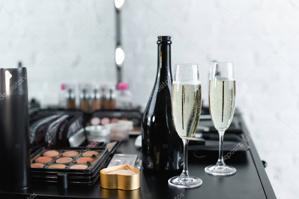 close up view of bottle and glasses of champagne on tabletop with cosmetics for makeup