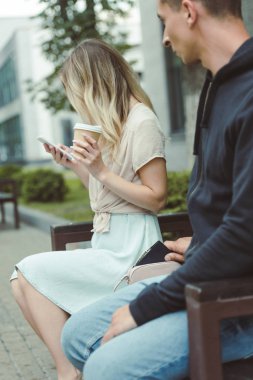 man pickpocketing purse from bag of woman sitting on bench in park   clipart