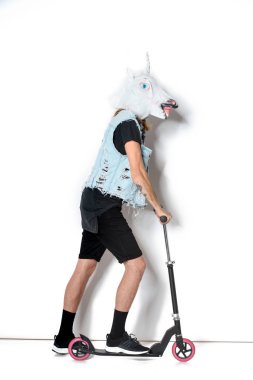 Beyaz adam tek boynuzlu maske ve denim yelek binme scooter yan görünüm