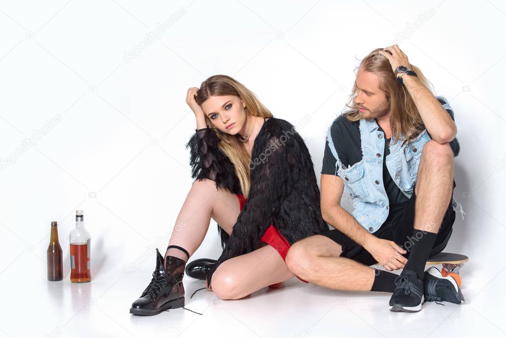 young drunk couple sitting on floor with bottles of alcohol on white