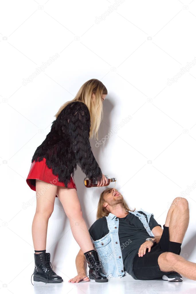 young woman pouring rum into mouth of boyfriend while he lying on floor on white