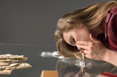 side view of addicted young woman sniffing cocaine from glass table clipart