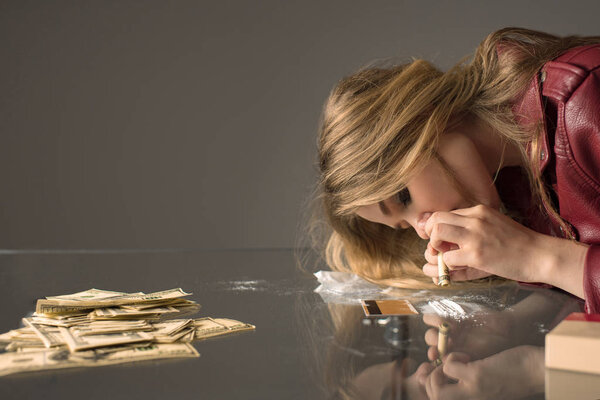 side view of young female junkie sniffing cocaine from glass table