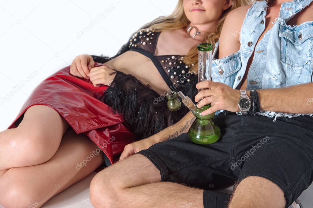 young high couple sitting on floor with water pipe of cannabis on white