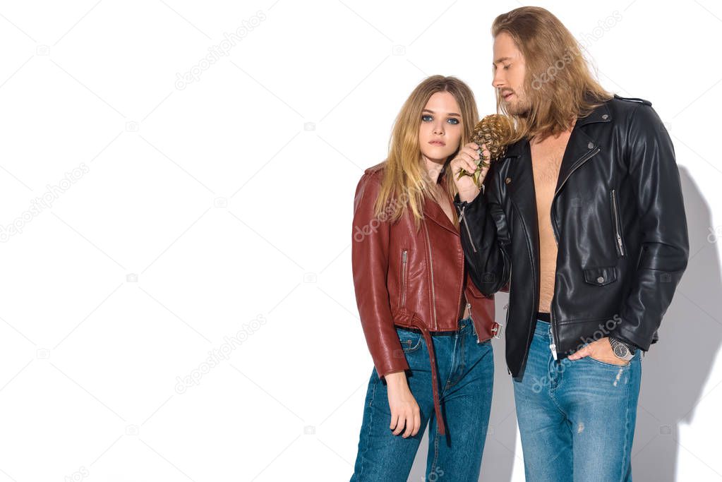 attractive young couple in leather jackets with pineapple standing together on white