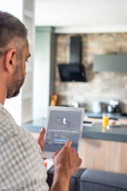 Selective focus of man using digital tablet with tumblr logo on screen in kitchen clipart