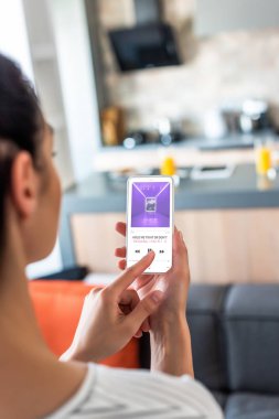 selective focus of woman using smartphone in kitchen clipart