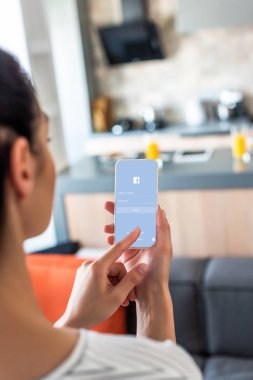 selective focus of woman using smartphone with facebook logo in kitchen clipart