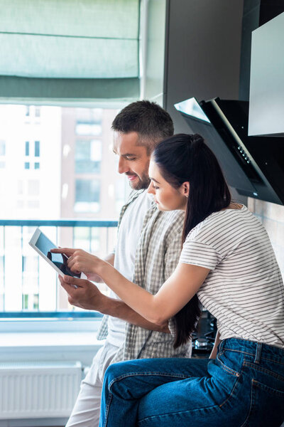 side view of married couple using digital tablet together in kitchen, smart home concept