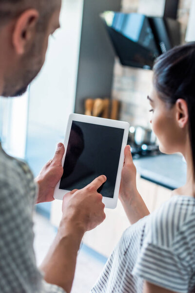 partial view of married couple using digital tablet with blank screen together at home, smart home concept