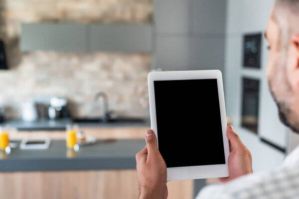 selective focus of man holding tablet with blank screen in hands in kitchen
