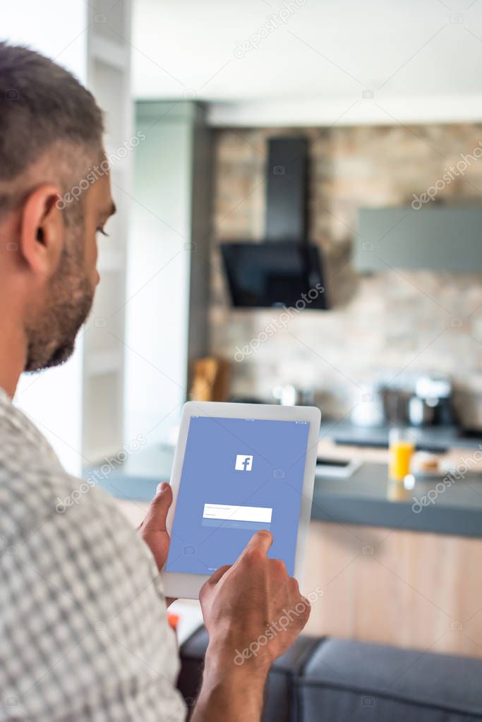 Selective focus of man using digital tablet with facebook logo on screen in kitchen