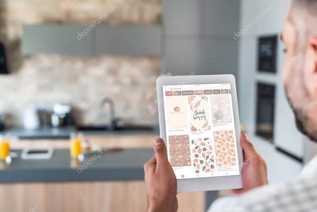 Selective focus of man using digital tablet with pinterest website on screen in kitchen