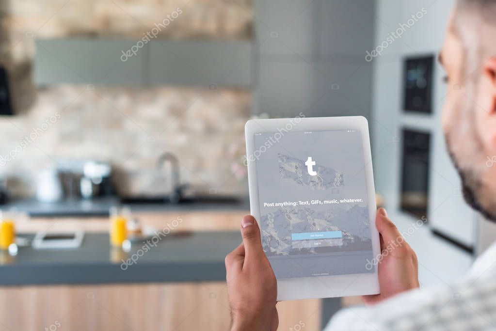 Selective focus of man using digital tablet with tumblr logo on screen in kitchen
