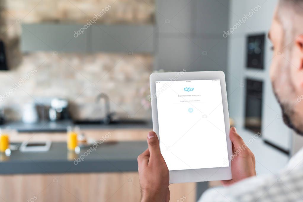 Selective focus of man using digital tablet with skype logo on screen in kitchen