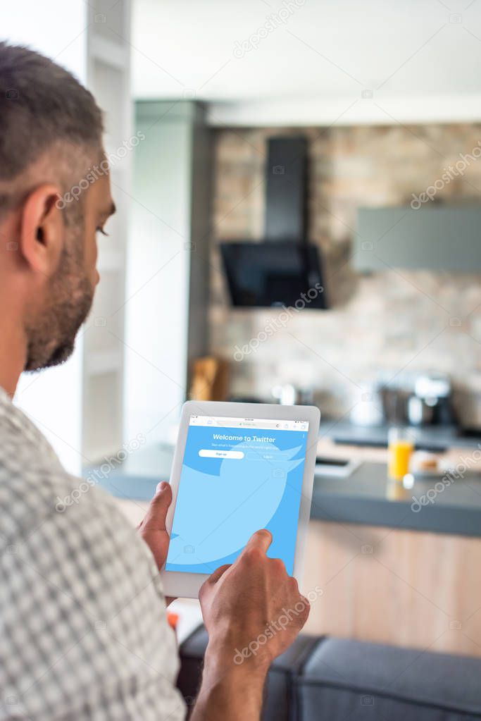 Selective focus of man using digital tablet with twitter logo on screen in kitchen