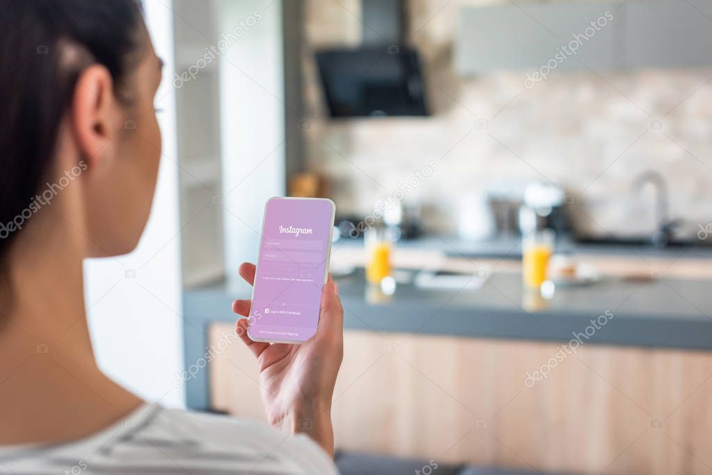Selective focus of woman holding smartphone with instagram logo on screen in kitchen