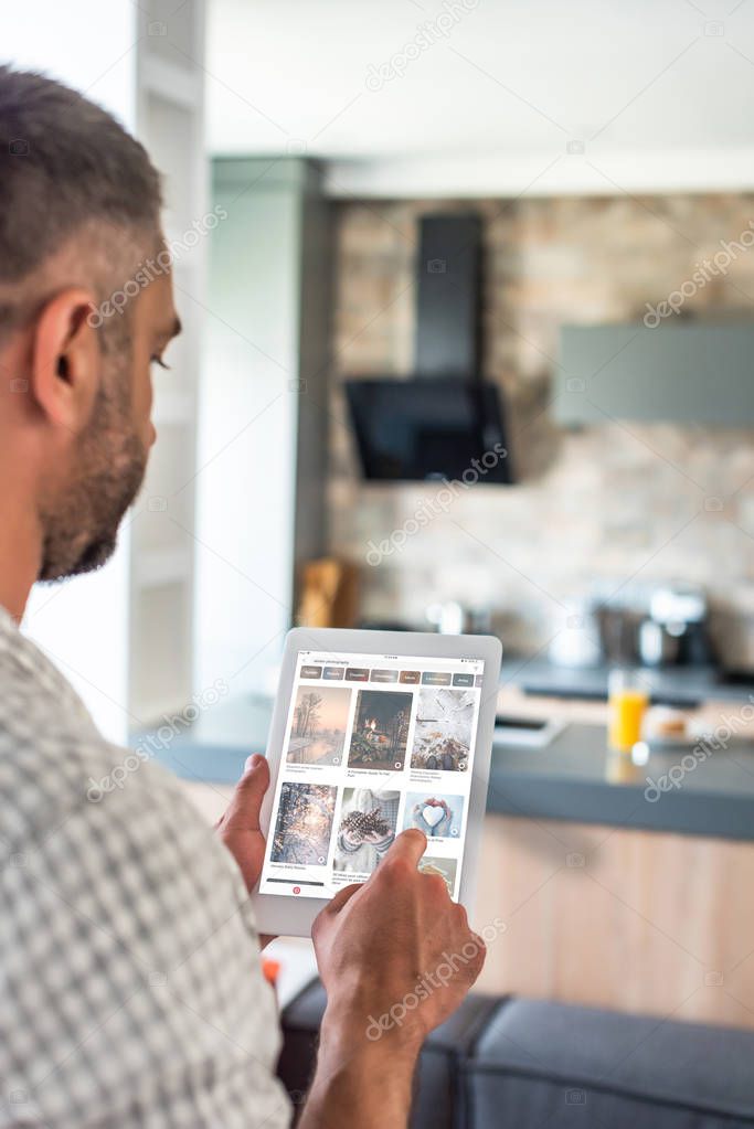 Selective focus of man using digital tablet with pinterest website on screen in kitchen