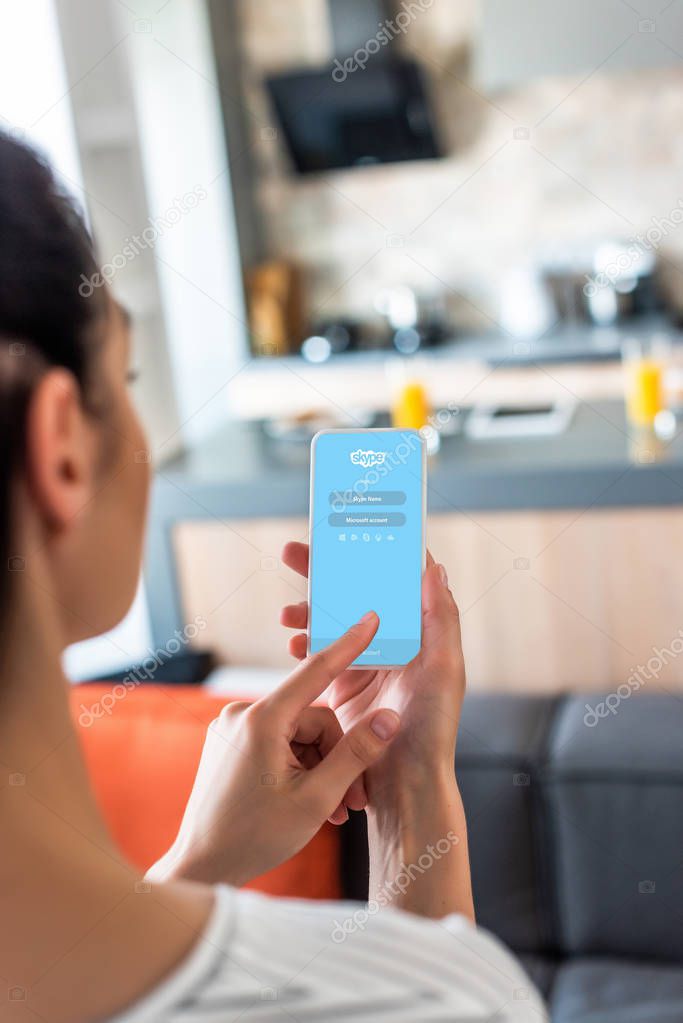 Selective focus of woman using smartphone with skype logo in kitchen