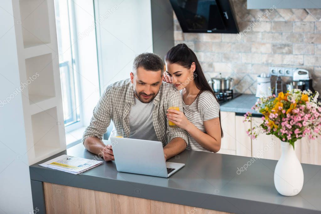 portrait of married couple using laptop together at counter in kitchen