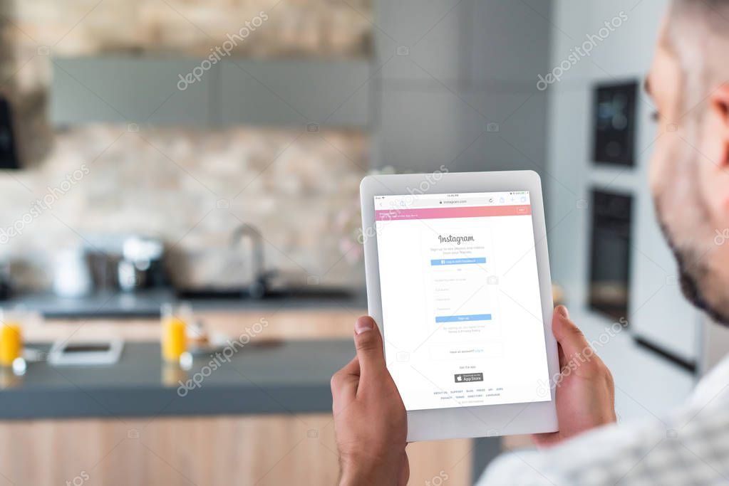 Selective focus of man using digital tablet with instagram logo on screen in kitchen