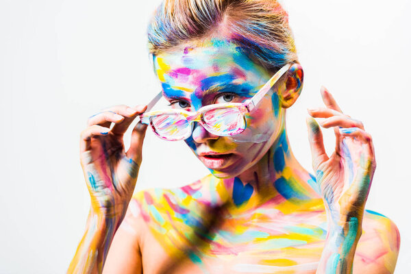attractive girl with colorful bright body art looking above sunglasses isolated on white