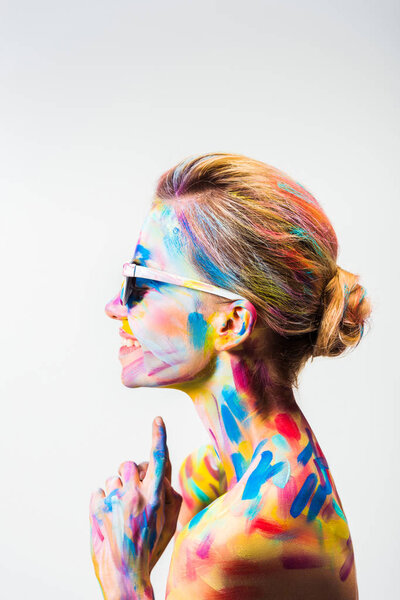 side view of smiling attractive girl with colorful bright body art and sunglasses isolated on white
