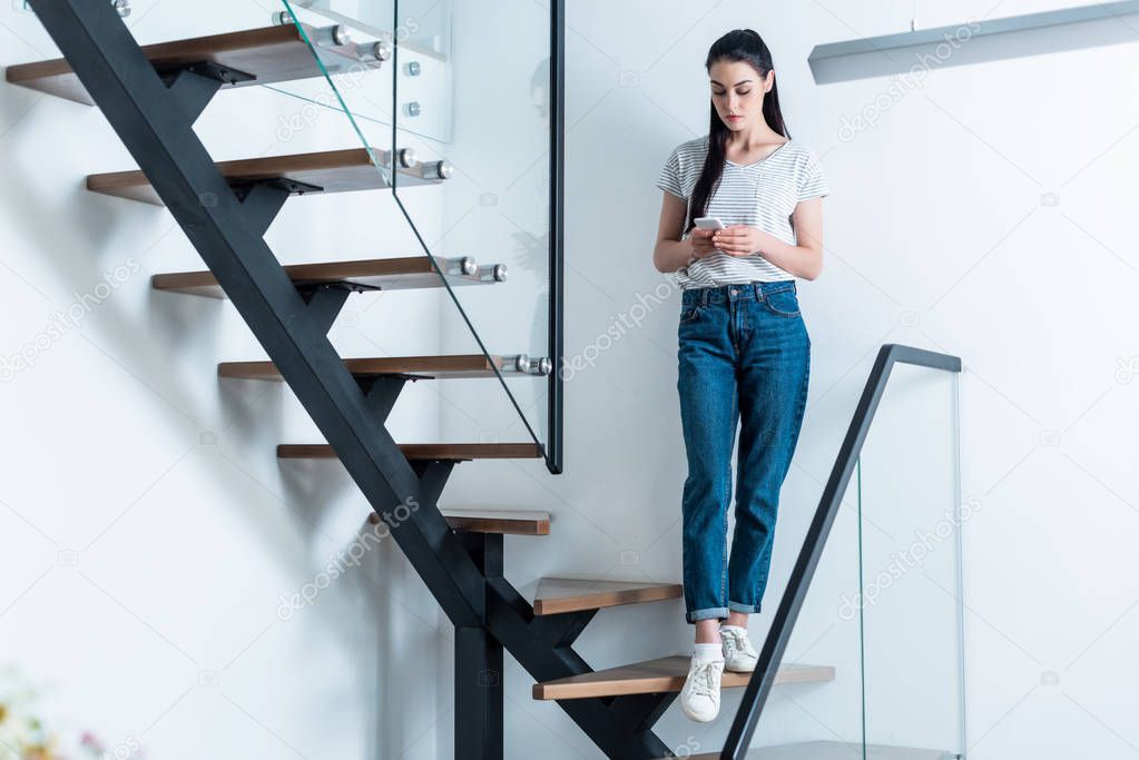 woman using smartphone while standing on stairs at home