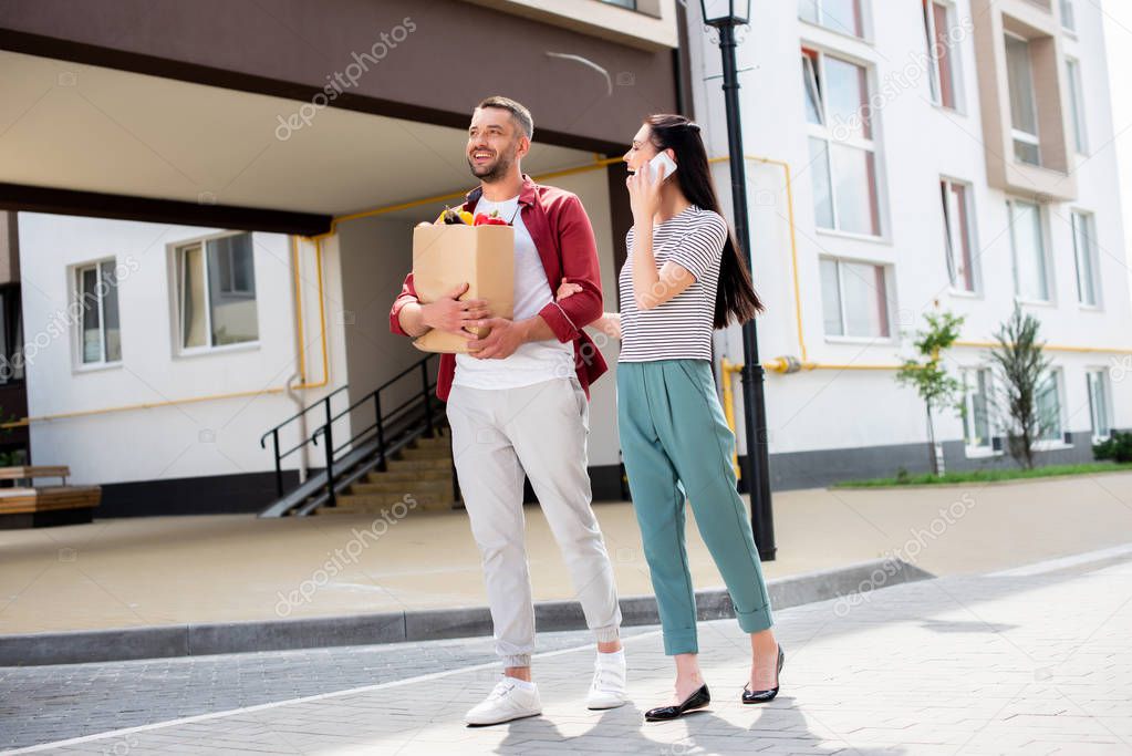 woman talking on smartphone while walking together with husband after shopping on street