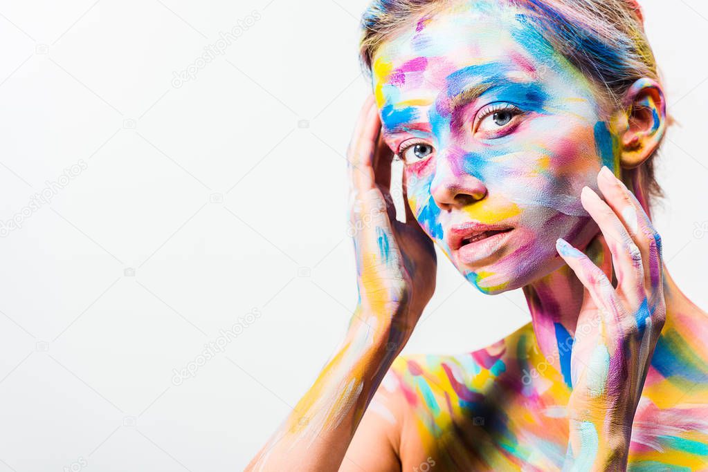 attractive girl with colorful bright body art touching face and looking at camera isolated on white 