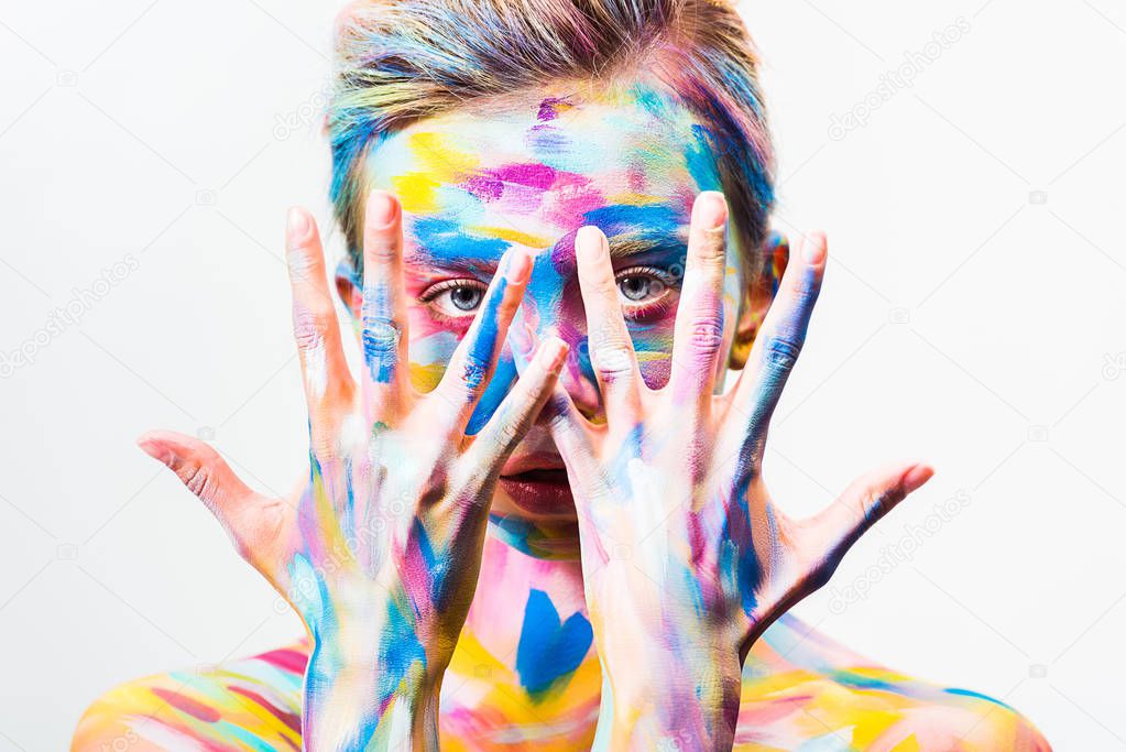 attractive girl with colorful bright body art looking at camera through fingers isolated on white 