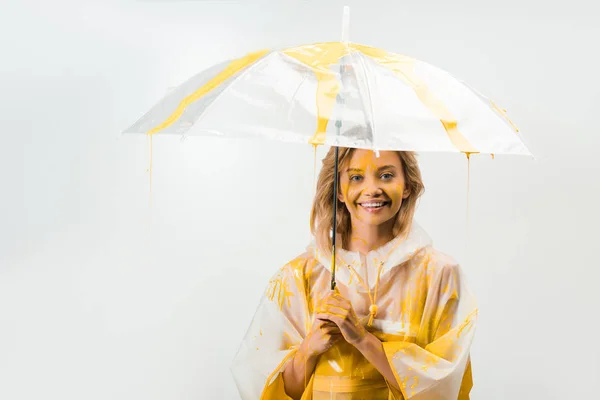 白で隔離傘の下で立っている黄色塗料で描かれたレインコートで笑顔の魅力的な女性  — 無料ストックフォト