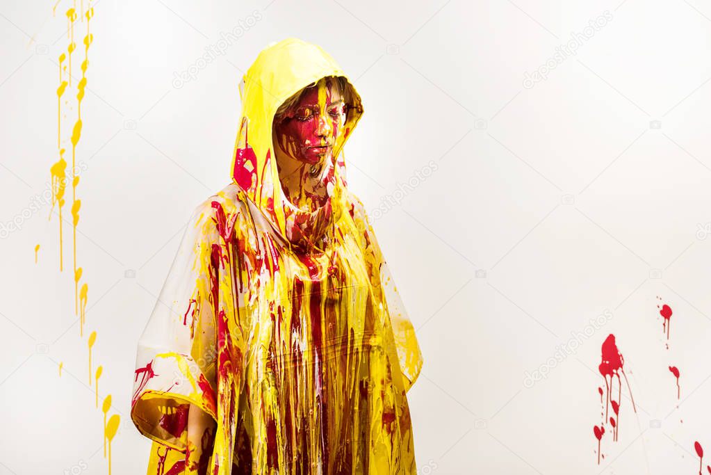 beautiful woman in raincoat painted with yellow and red paints standing with closed eyes isolated on white