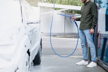 cropped image of man cleaning car at car wash with high pressure water jet clipart