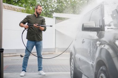 side view of handsome man cleaning car at car wash with high pressure water jet clipart